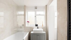 A bathroom with a bathtub, a sink, and a window. - New! Modern 2BR House w/ Patio in Acton (Greater London)