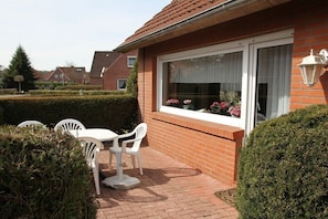 Ein Wohnhaus mit Backsteinfassade, einem Fenster mit weißem Vorhang und einer kleinen Terrasse mit Tisch und Stühlen.