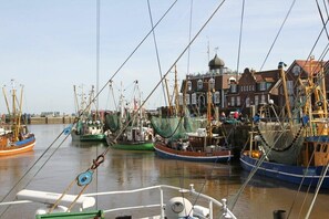 A harbor with multiple fishing boats docked, a building with a dome, and a clear sky. - Holiday apartment with 1 bedroom (Esens\/Moorweg-Wagnersfehn)