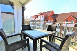 Ein Balkon mit einem Glastisch und Korbstühlen, mit Blick auf eine Reihung von Häusern mit roten Dächern.