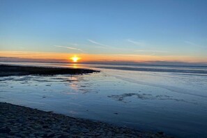 Ein Strandbild bei Sonnenuntergang, ruhiges Wasser und Kieselsteine.