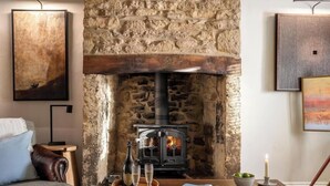 A stone fireplace with a modern stove, a cozy seating area with a leather armchair, and a framed artwork on the wall.