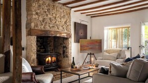 A cozy living room with a stone fireplace, wooden beams, a sofa, and a painting.