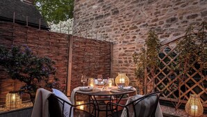 An outdoor dining area with wicker furniture, candles, and a stone wall backdrop.