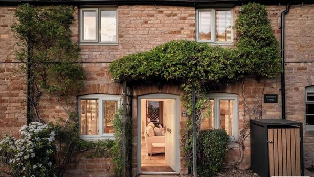 A stone building with ivy-covered walls, a wooden door, and a sign indicating 'Chiltern's Cottage.'