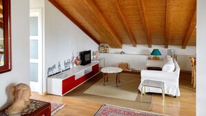 Ett vardagsrum med ett träpanelat tak, en vit soffa, en röd och vit konsol och ett litet bord med en lampa.