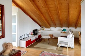 A living room with a wooden ceiling, white sofa, red and white console, and a small table with a lamp. - 'Nido in Città' Room with Mountain View, Private Garden and Air Conditioning (Udine)