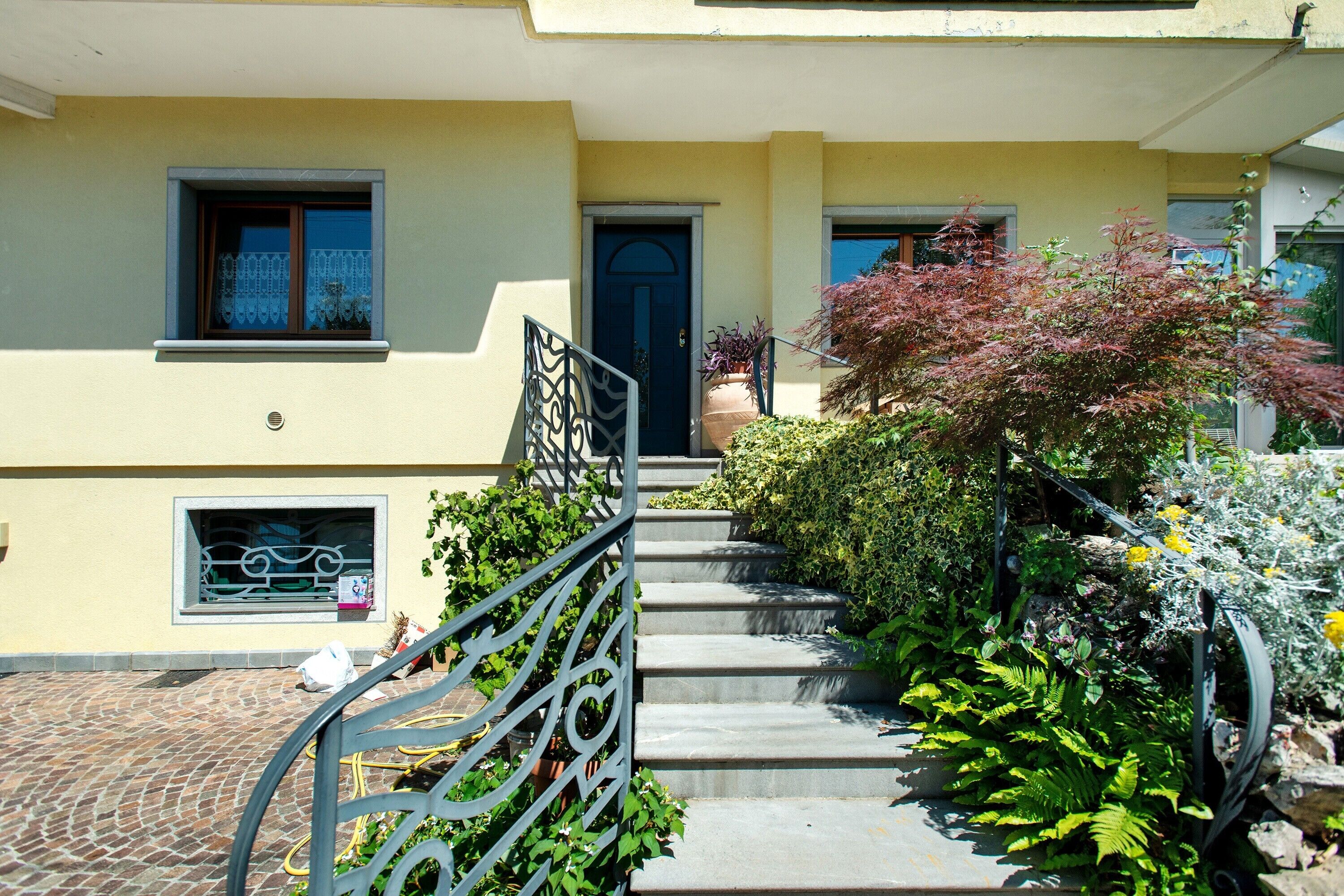 Un immeuble résidentiel avec un escalier menant à une porte, entouré de verdure et doté d’une rambarde en métal.