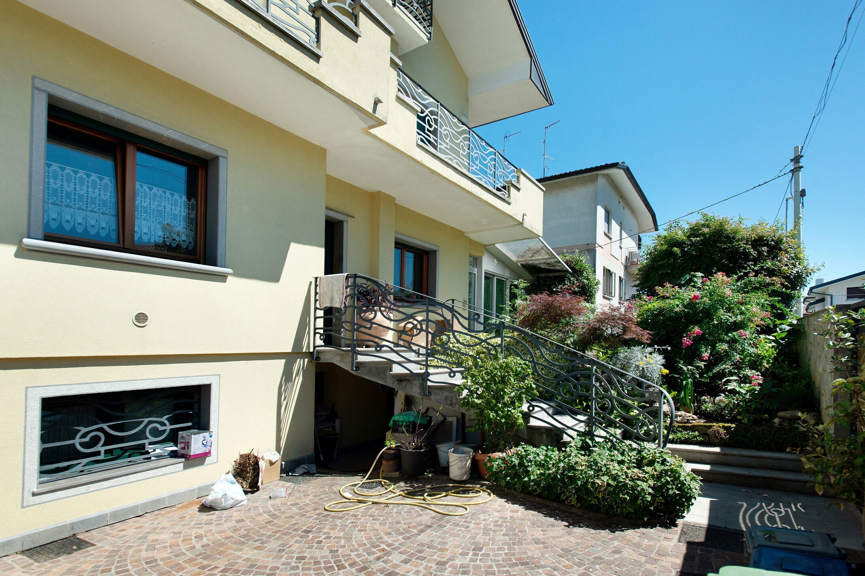 A multi-story building with balconies, a staircase, and a garden area with potted plants.