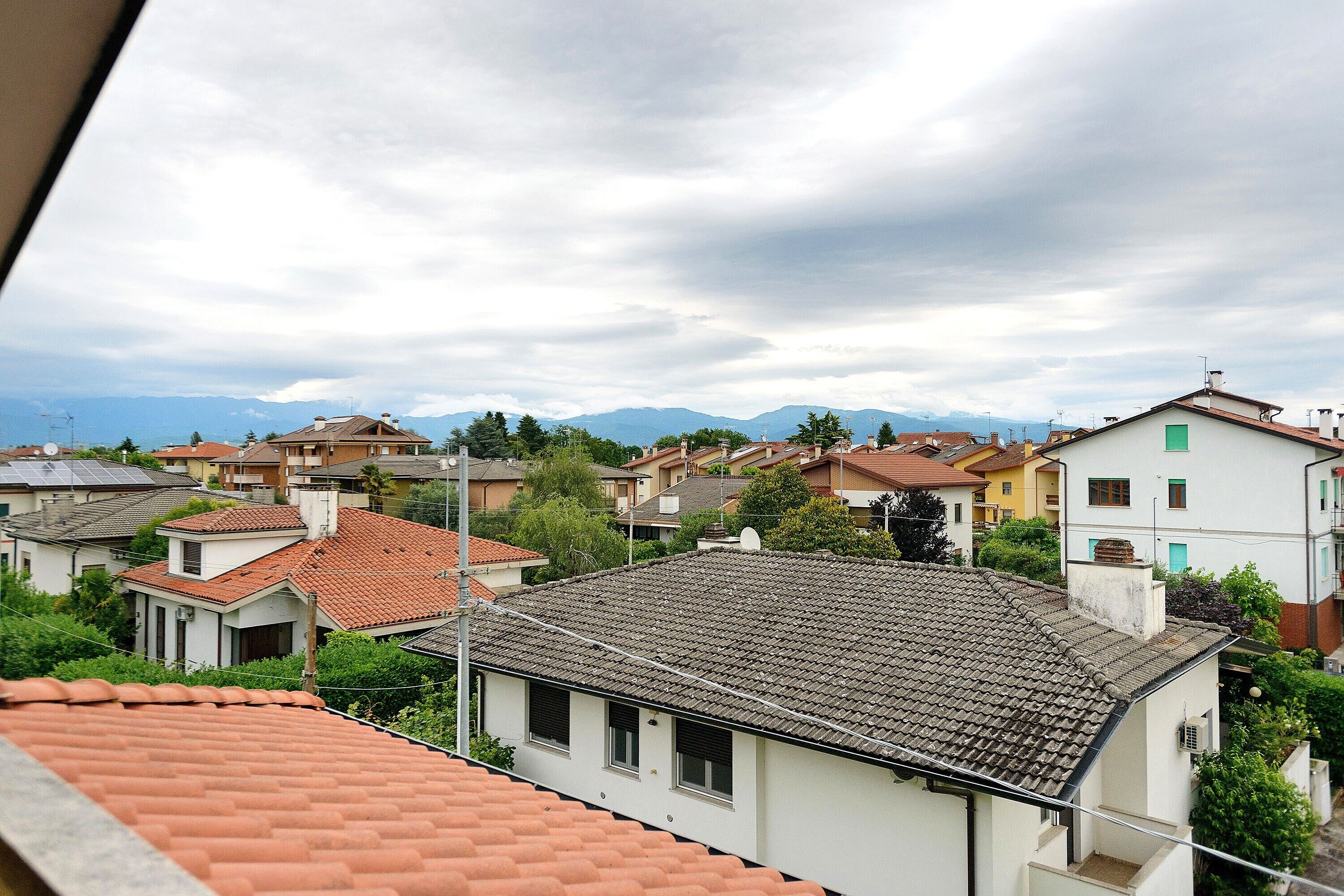 Un quartier résidentiel avec des maisons, dont certaines ont des toits recouverts de tuiles rouges, et une chaîne de montagnes en arrière-plan.