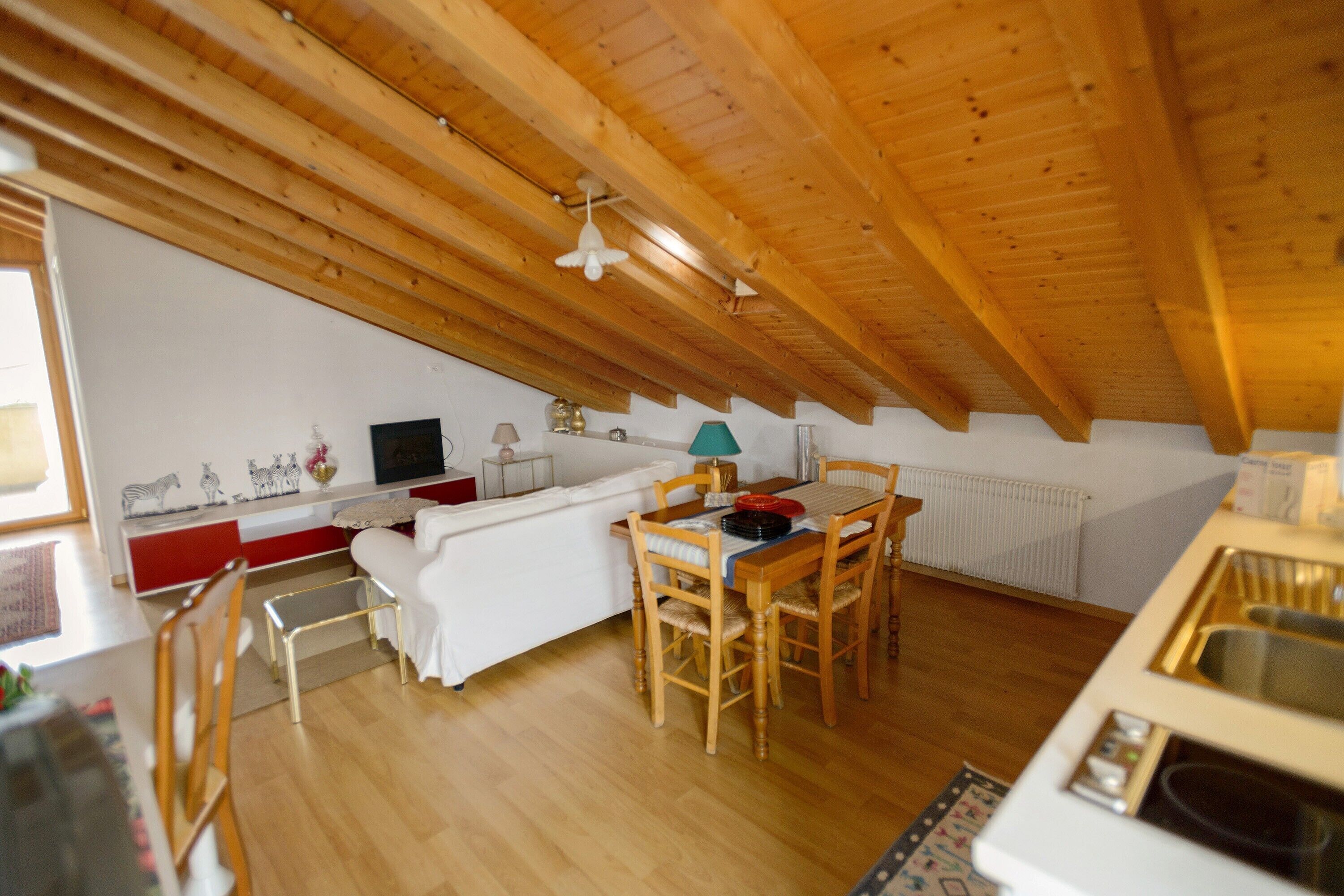 Une pièce mansardée chaleureuse avec un plafond en bois, une table à manger avec des chaises, un canapé et un petit coin cuisine.