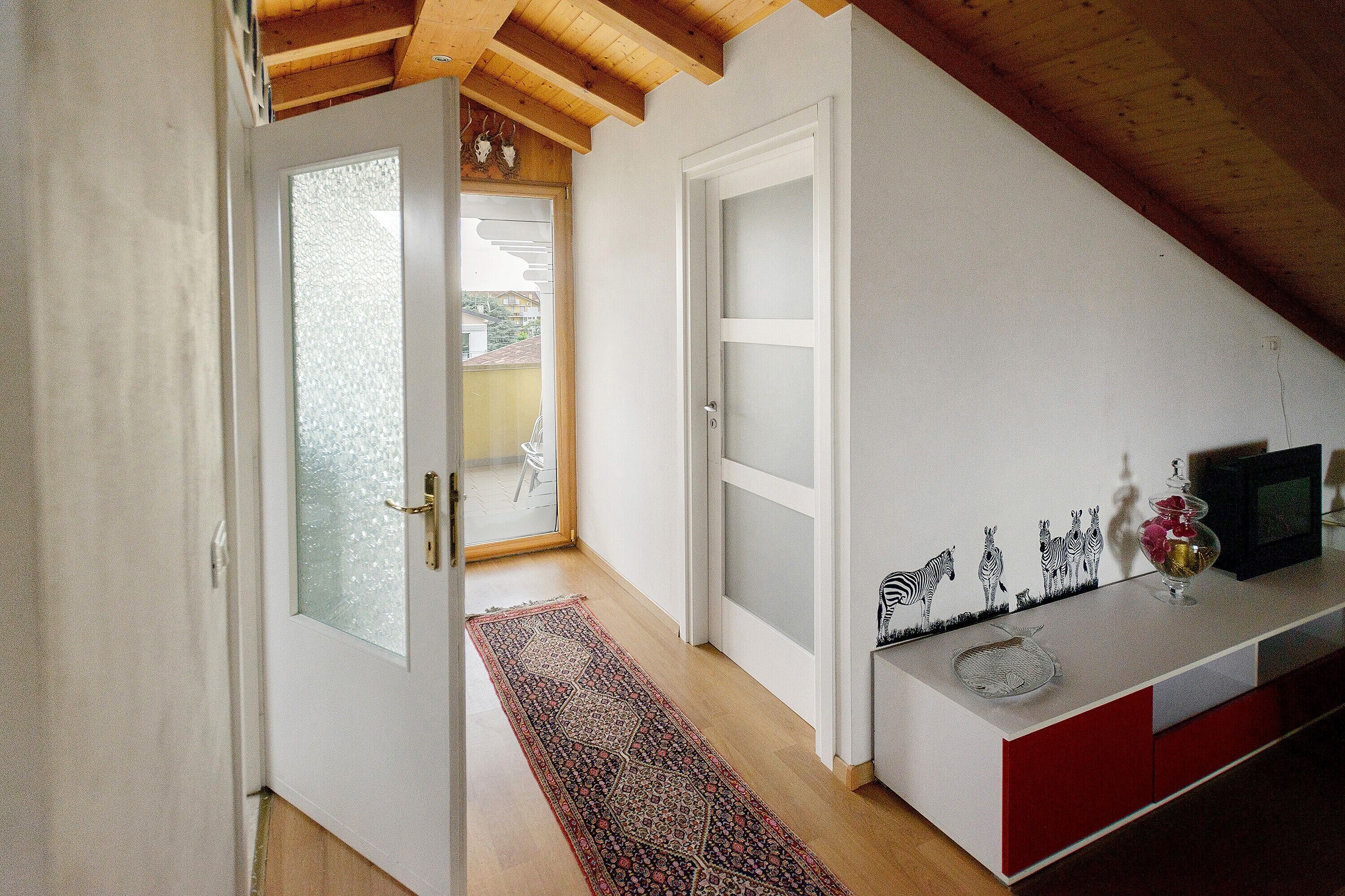 A hallway with a wooden ceiling, a white door, a red cabinet, and a small table with decorative items.