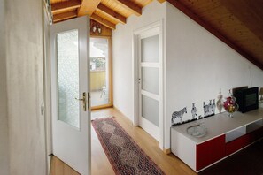 A hallway with a wooden ceiling, a white door, a red cabinet, and a small table with decorative items. - 'Nido in Città' Room with Mountain View, Private Garden and Air Conditioning (Udine)