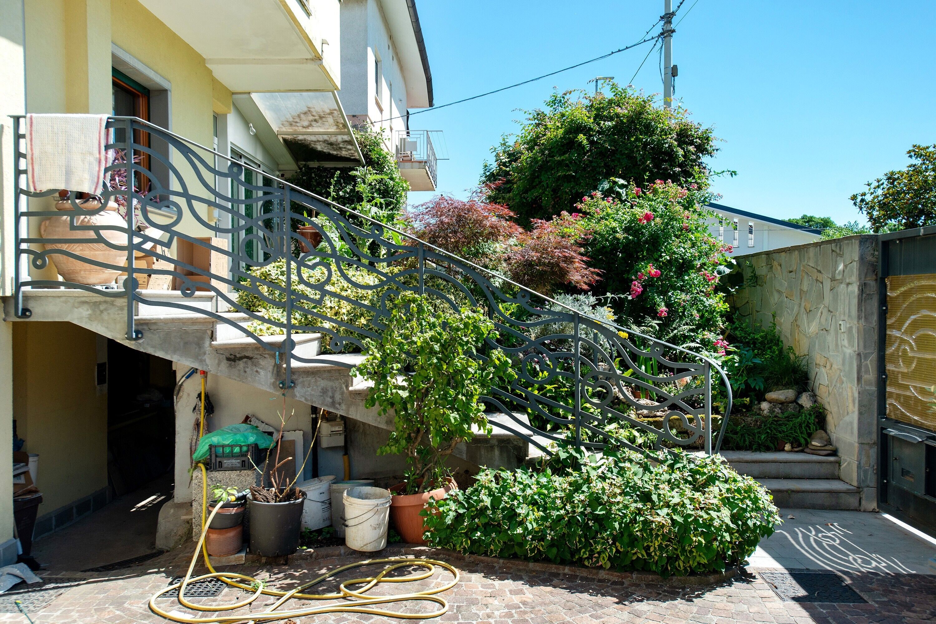 Une cour avec un escalier en métal, des plantes en pot et un mur de pierre.