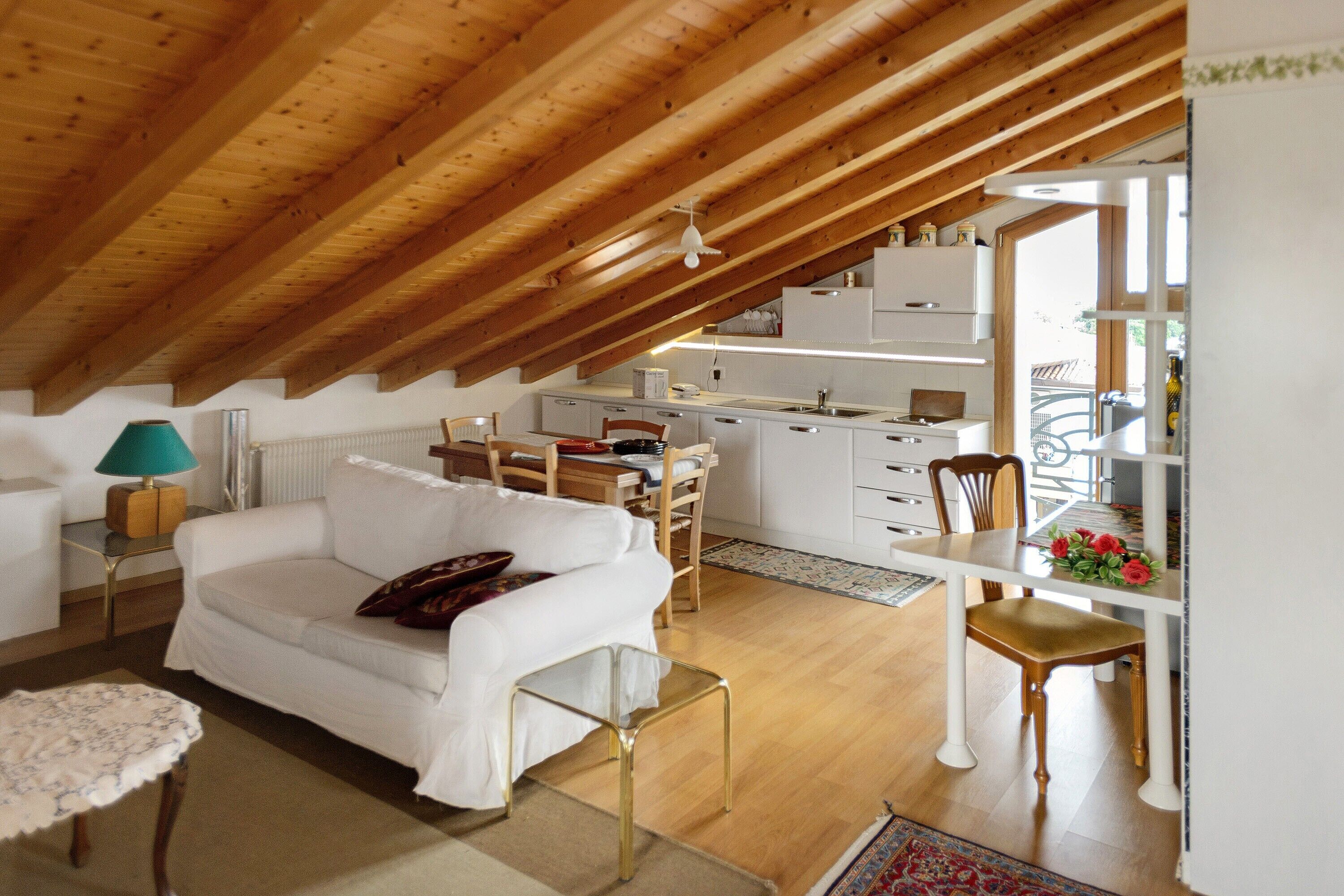 Un espacio habitable estilo loft con techo alto, vigas de madera, un sofá blanco, una mesa de comedor y una zona de cocina.
