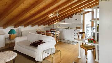 Un espacio habitable estilo loft con techo alto, vigas de madera, un sofá blanco, una mesa de comedor y una zona de cocina.