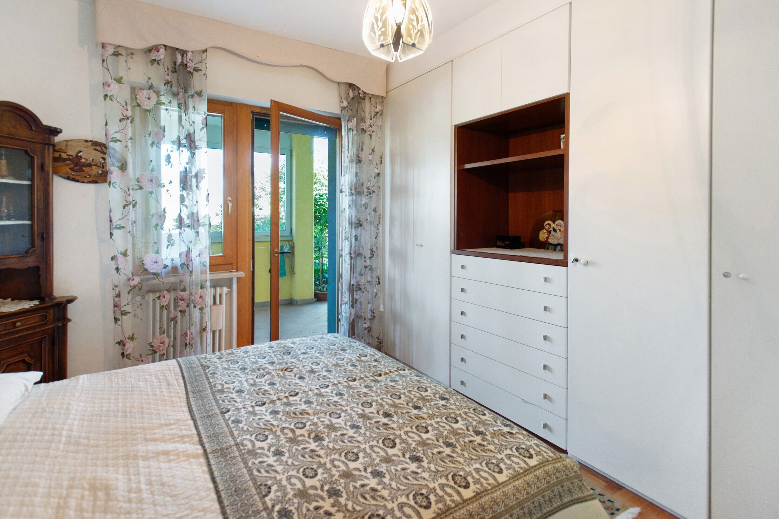 A bedroom with a bed, a dresser, a wardrobe, and a window with curtains.