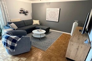 Ein Wohnzimmer mit Sofa, Sessel, Couchtisch und einem Kunstwerk an der Wand.