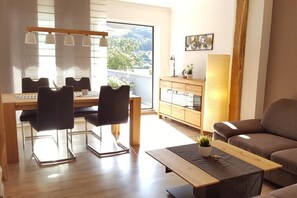 Ein modernes Wohnzimmer mit Essbereich, einer Couch, einem Couchtisch und Blick ins Freie.