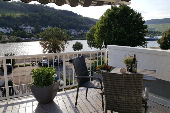 Ein Balkon mit Korbstühlen, einer Topfpflanze und einer Weinflasche.