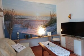En stue med et stort maleri af en strand, et fjernsyn, et træbord og en sofa.