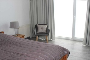 Ein Schlafzimmer mit Bett, Stuhl, Lampe und Blick ins Freie.
