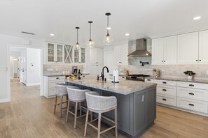 Una cocina moderna con armarios blancos, una isla grande con taburetes de bar, iluminación colgante y una campana extractora de acero inoxidable.