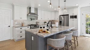 Une cuisine moderne avec des meubles blancs, un grand îlot central doté de tabourets, des appareils en acier inoxydable et un éclairage suspendu.