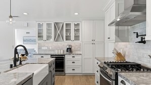 Une cuisine moderne avec des meubles blancs, un four encastré, une cuisinière à gaz et une machine à café.