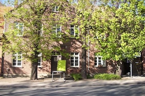 Ein Backsteinhaus mit vielen Fenstern, einem grünen Stuhl und Bäumen davor.