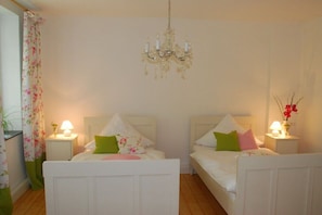 Ein Schlafzimmer mit zwei Betten, einer Chandelüster, Nachttischlampen und blumigen Vorhängen.