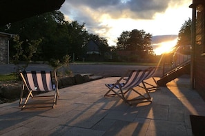 Zwei gestreifte Lounge-Sessel auf einer gepflasterten Terrasse mit Sonnenuntergang im Hintergrund.
