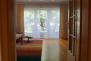 Ein Zimmer mit großem Fenster, einem Sessel, einem Tisch und Holzboden.