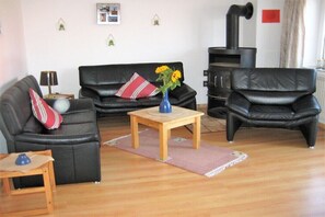 Ein Wohnzimmer mit einer schwarzen Ledersofa, einem kleinen Holztisch mit Blumenvase, einem schwarzen Kamin und einem roten Schild an der Wand.