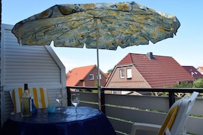 Ein Balkon mit Tisch, Sonnenschirm und einer Weinflasche.