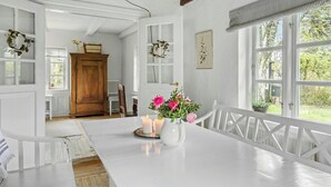 Une pièce avec un plafond en bois, des murs blancs, une grande fenêtre, une table blanche ornée de bougies et un vase rempli de fleurs.