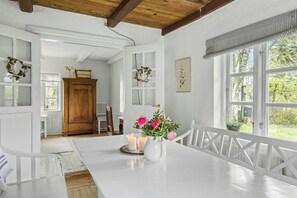 A room with a wooden ceiling, white walls, a large window, a white table with candles, and a vase with flowers. - Country farmhouse close to the beach (Hals)