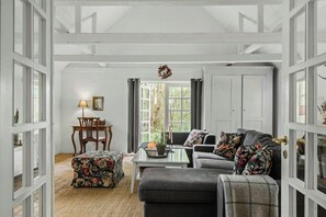 A room with a dining table, chairs, a sofa, and a window with curtains. - Country farmhouse close to the beach (Hals)