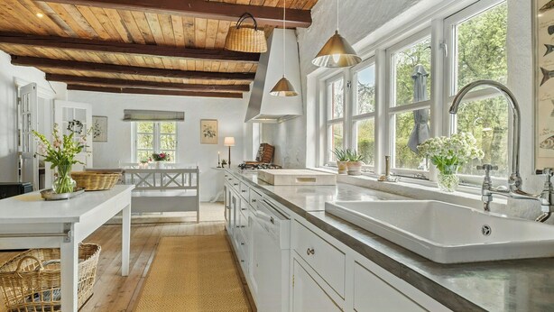 Une cuisine avec des meubles blancs, un grand évier, des luminaires suspendus et un plafond en bois.