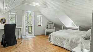 Une chambre avec un plafond en pente, un lit, une chaise, un bureau et une fenêtre.