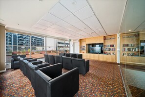 Een bibliotheek met zwarte lederen fauteuils, boekenkasten, een televisie en een kamerbreed tapijt met dessin.
