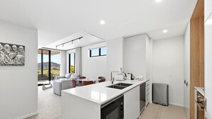 Cozinha moderna com ilha central, área de jantar com vista e sala de estar com sofá e cadeiras.