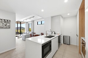 A modern kitchen with a central island, a dining area with a view, and a living space with a sofa and chairs. - Tranquil 2-Bed with Water View (Kingston)
