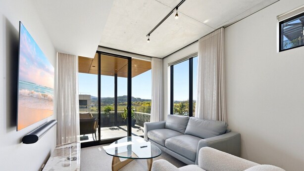 Sala moderna com mesa de centro de vidro, sofá cinza e uma grande janela com vista para o exterior.