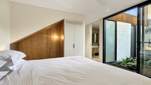 Et soveværelse med en seng, et træhovedgærde, et hvidt klædeskab og en skydedør af glas, der fører ud til en balkon.