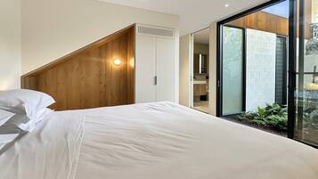 Ein Schlafzimmer mit einem Bett, einem Holzkopfstück, einem weißen Kleiderschrank und einer Glastür zum Balkon.
