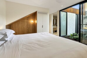 Ein Schlafzimmer mit einem Bett, einem Holzkopfstück, einem weißen Kleiderschrank und einer Glastür zum Balkon.