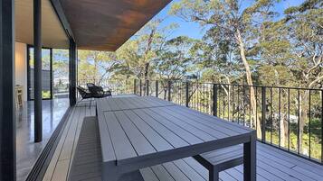 A wooden deck with a table and chairs, a metal railing, and a view of trees.