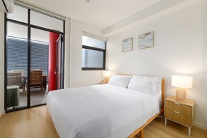 Un dormitorio con cama, mesitas de noche, ventana y puerta corrediza que da a un espacio exterior.