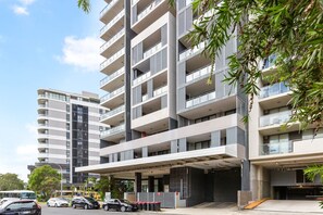 A multi-story building with balconies, a covered entrance, and a parking area. - Modern 2-Bed Apartment Near Airport (Wolli Creek)